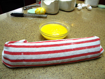 cake rolled up in the kitchen towel, curd cooking in bowl.